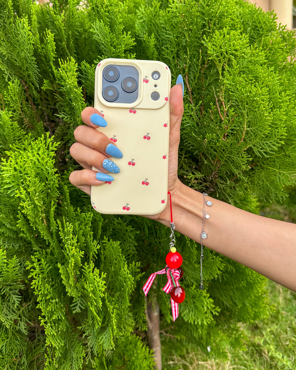 TOKFO Cherry iPhone phone case in cream with red cherry print and cherry charm, held in hand