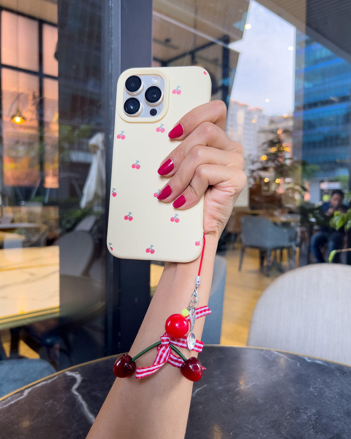 TOKFO Cherry cream iPhone phone case with red cherry print, held up with the cherry charm hanging below