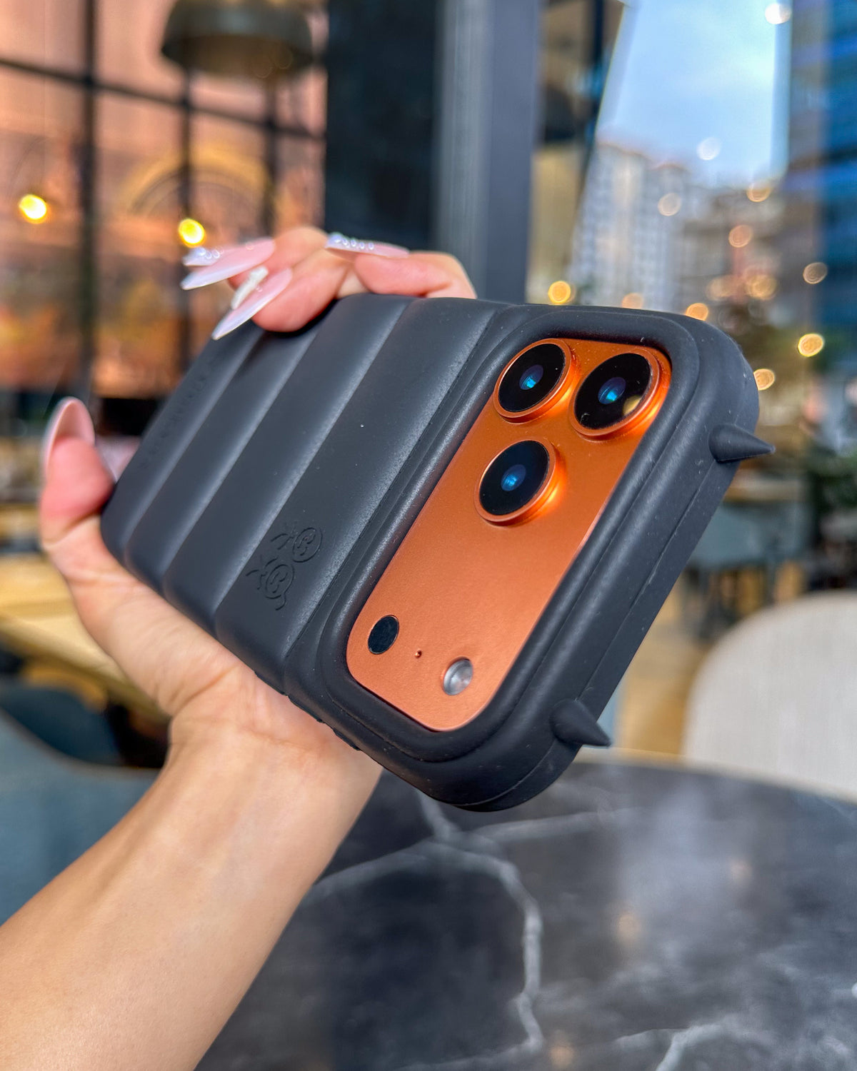 Black TOKFO Puffer Devil Horn phone case on an orange iPhone showing the 3D devil horns on the camera ring