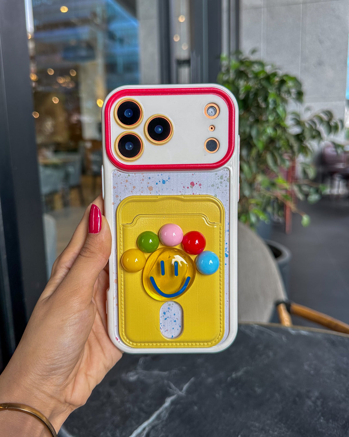 TOKFO Smiley iPhone phone case with 3D smiley face and colourful ball details, held in hand