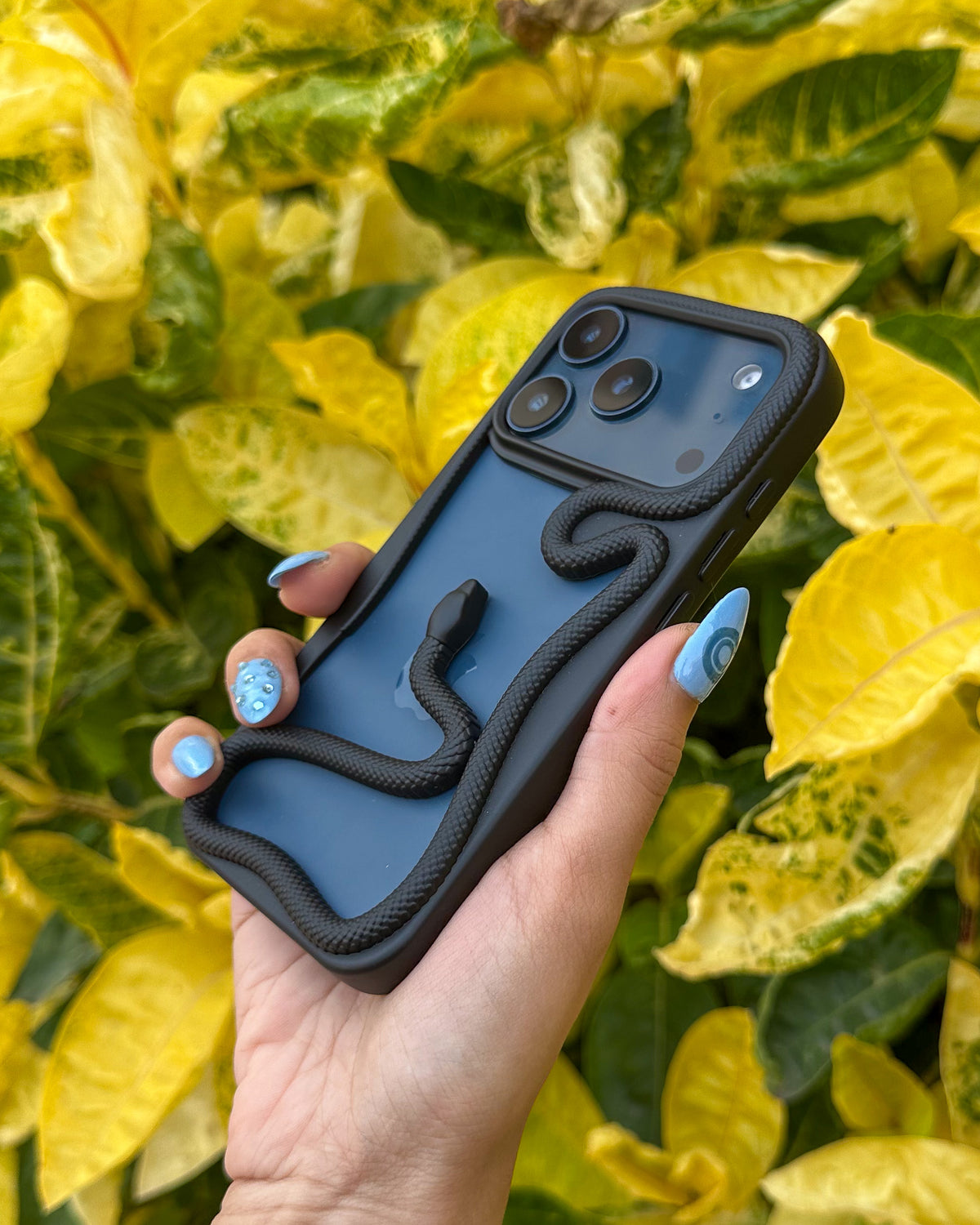 Black TOKFO Snake bumper phone case held at an angle in front of leaves